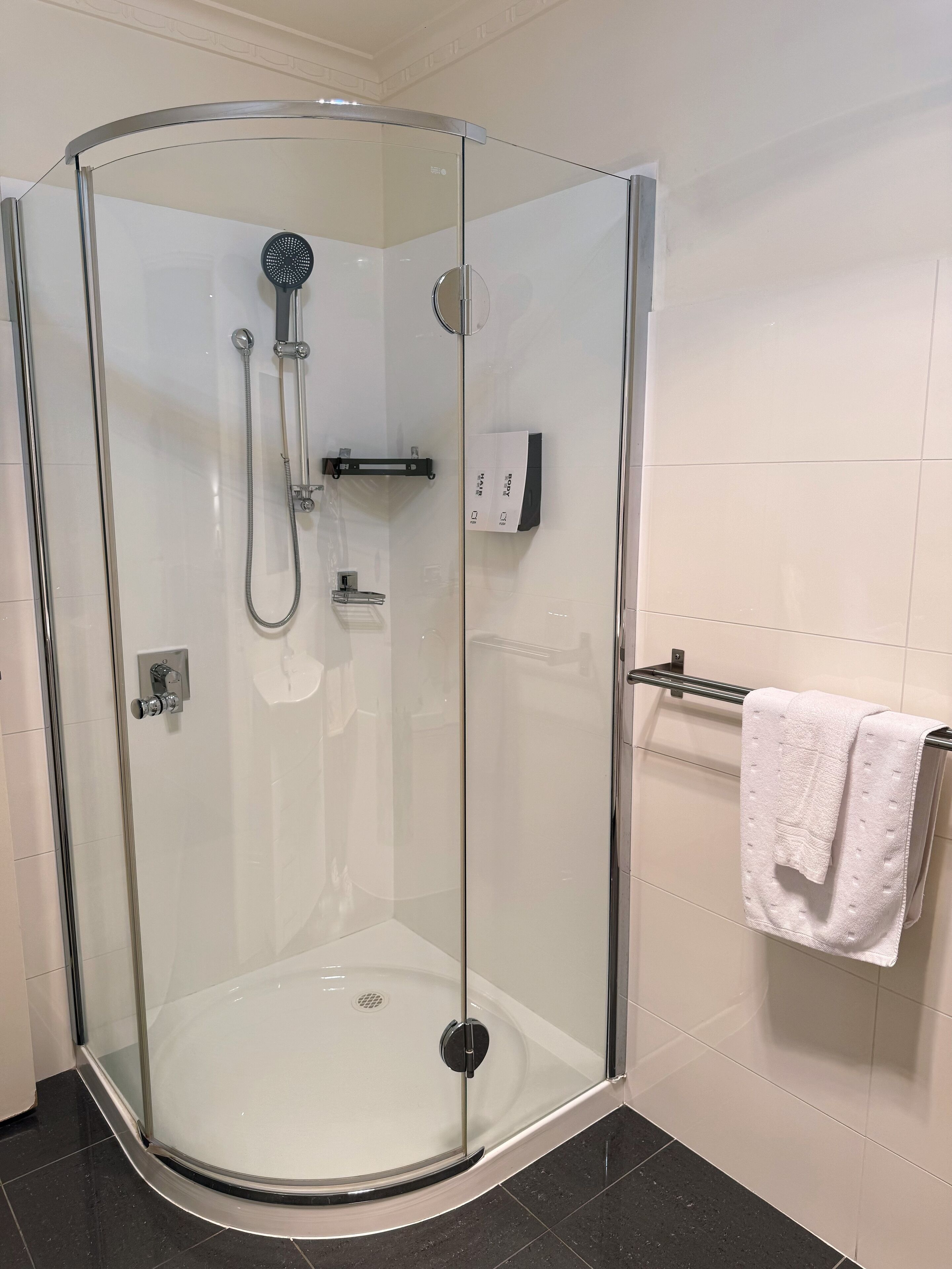 A glass-enclosed shower with a handheld showerhead and a wall-mounted control panel.