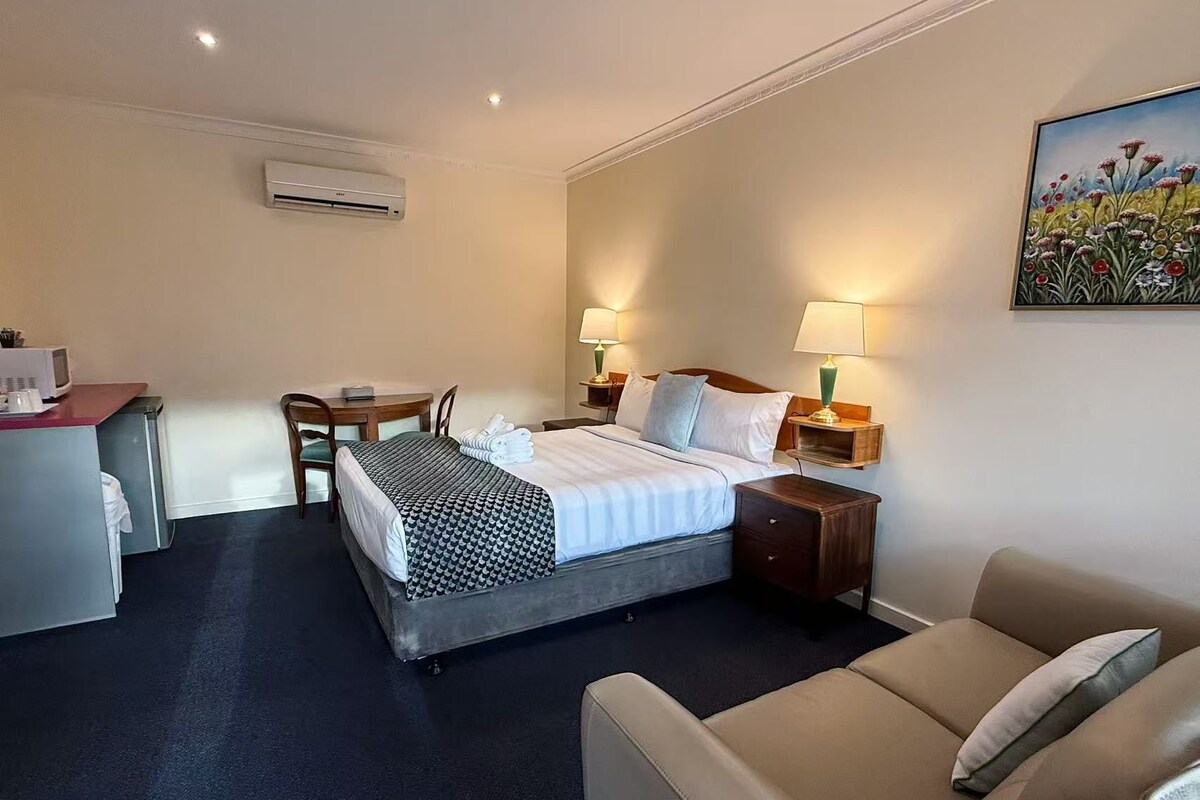 A hotel room with a bed, bedside tables, a desk, a chair, and a couch.
