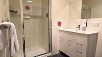 A modern bathroom with a glass-enclosed shower, white tiles, and a vanity with a mirror.