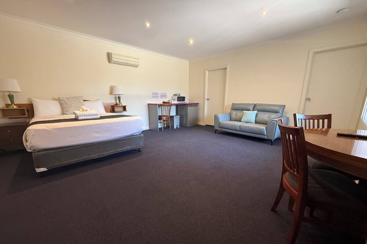 A hotel room with a bed, a desk, a sofa, and a dining table.