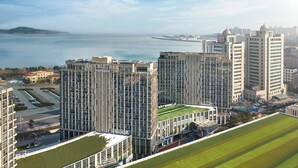 A high-rise hotel with multiple floors, a parking area, and a view of the sea.
