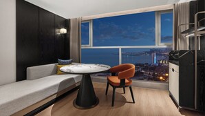 A modern room with a sofa, a table, and a chair, a large window with a city view, and a cityscape visible through the window.