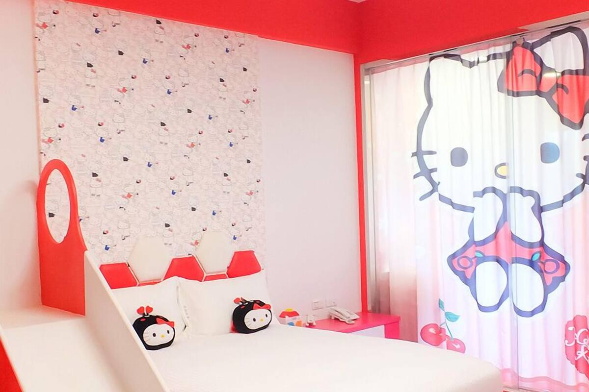 Une chambre avec un lit, un rideau à l’effigie de Hello Kitty et un mur orné d’un motif.