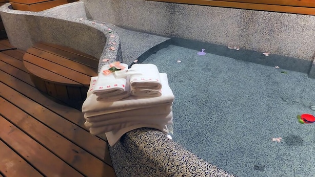 A wooden bench and a stone hot tub with towels stacked on it. - Tong's Story Paternity B&B (Hualien City)