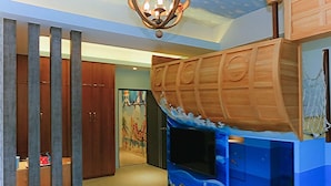 A room with a wooden boat-shaped play area, a ceiling light fixture, and a door with a colorful mural. - Tong's Story Paternity B&B (Hualien City)