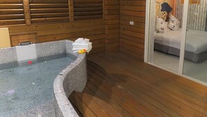 A wooden cabin with a stone bathtub, a wooden floor, and a bed with a white and gray bedspread. - Tong's Story Paternity B&B (Hualien City)