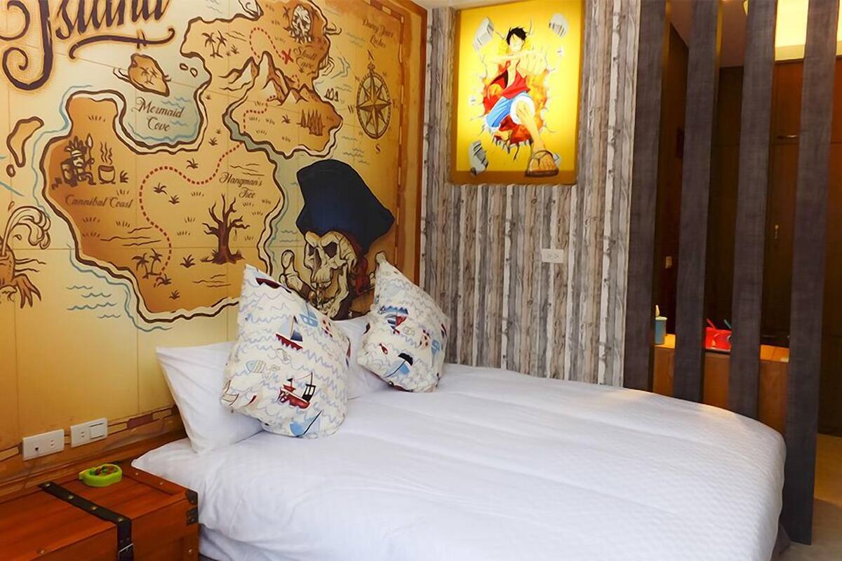 Une chambre d’hôtel avec une grande fresque représentant une carte, un lit avec une literie blanche et une affiche encadrée d’un personnage d’anime.