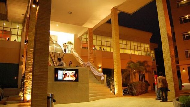 A hotel lobby with a central staircase, palm trees, and a TV screen. - Westerngrand Hotel Ratchaburi (Ratchaburi)