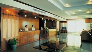 A hotel reception area with a wooden reception desk, a clock, and a TV. - Westerngrand Hotel Ratchaburi (Ratchaburi)