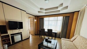A modern hotel room with a flat-screen TV, a dining area with a table and chairs, a sofa, and a large window with curtains. - Westerngrand Hotel Ratchaburi (Ratchaburi)