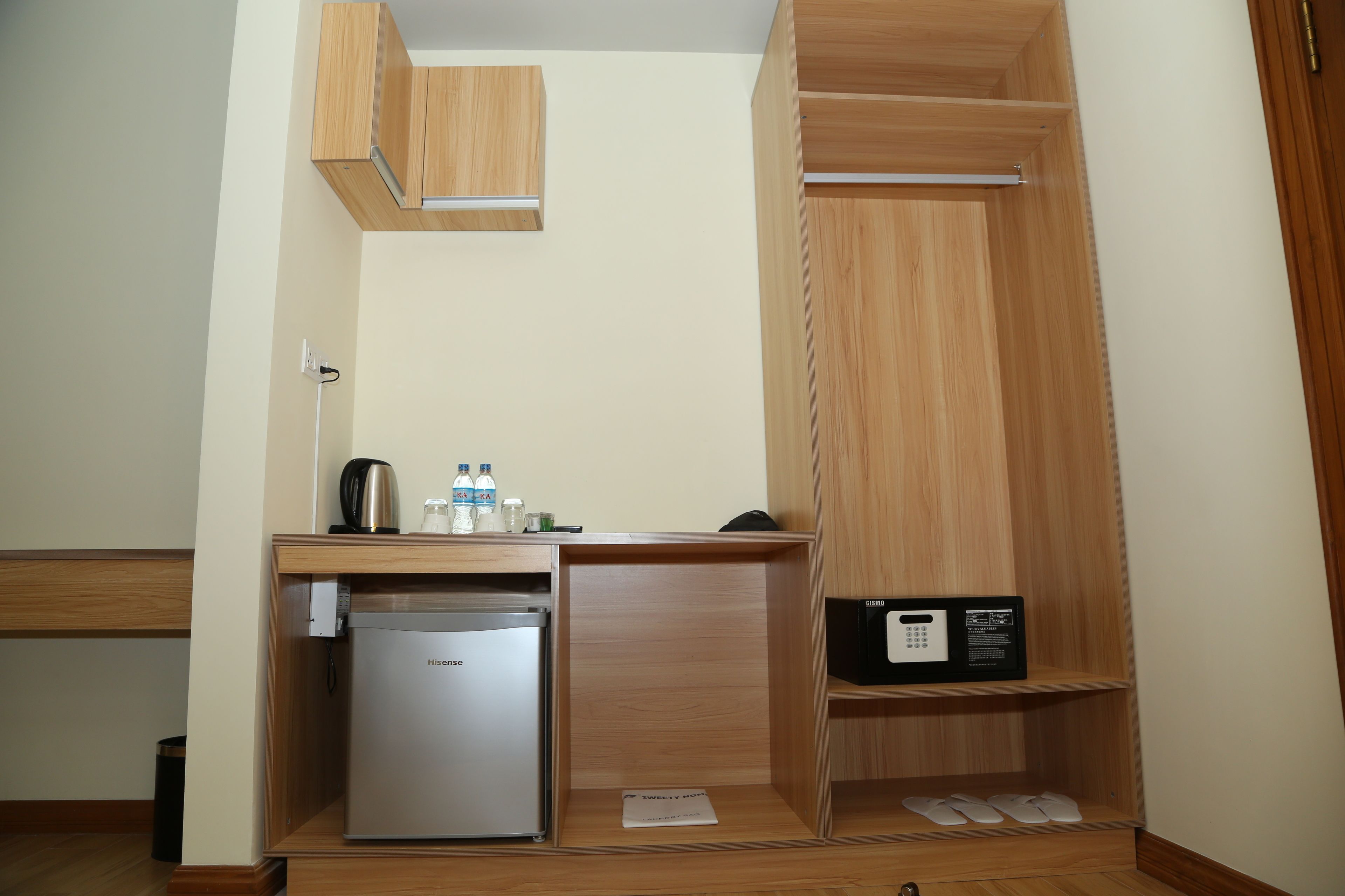 Una kitchenette compacta con refrigerador, microondas y una pequeña encimera con hervidor de agua, botellas de agua y cafetera.
