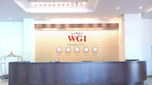 Un comptoir d’accueil à l’hôtel WGI, avec un mur recouvert de panneaux en bois, des horloges indiquant différents fuseaux horaires et un lustre au-dessus.