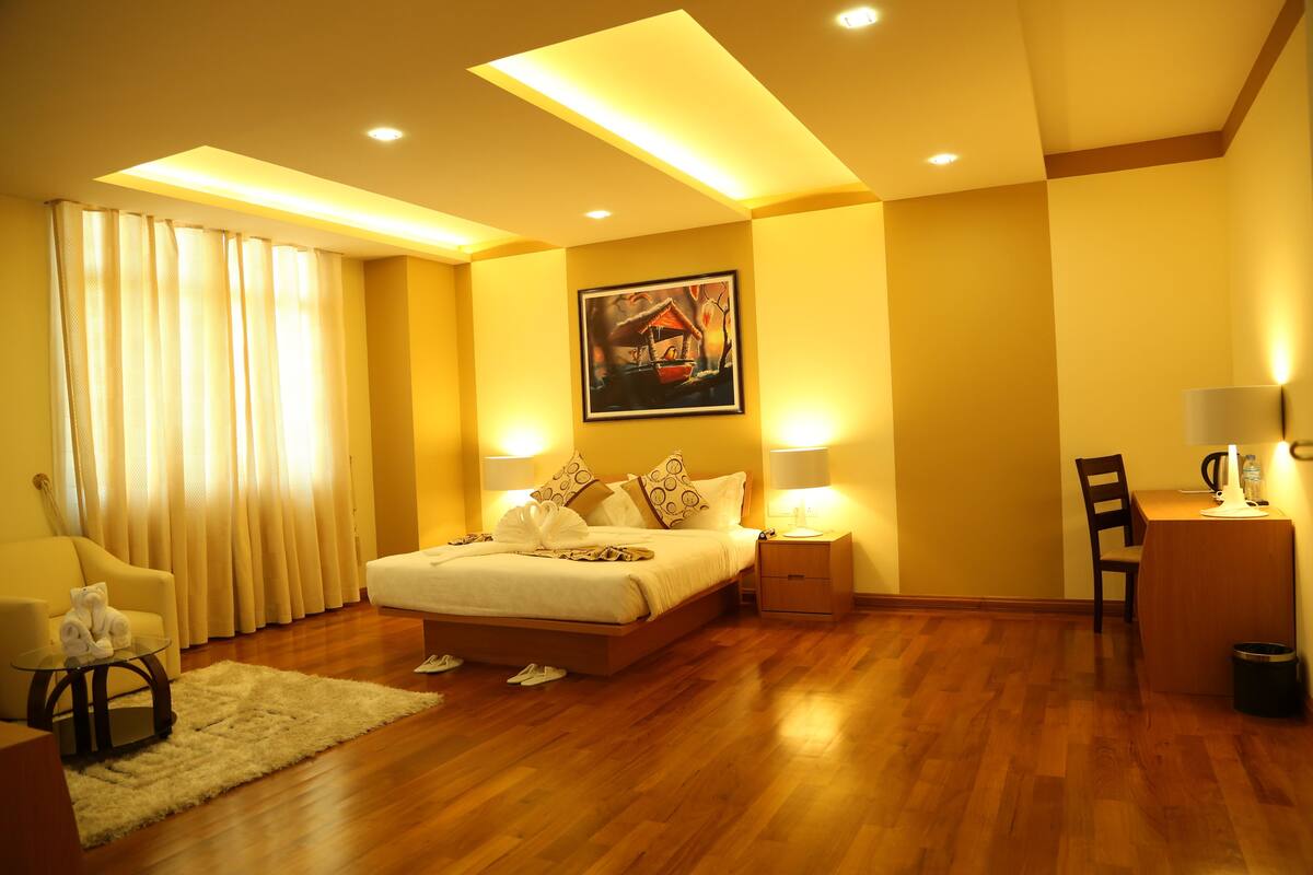 A hotel room with a bed, bedside tables, a desk, a chair, and a painting on the wall.