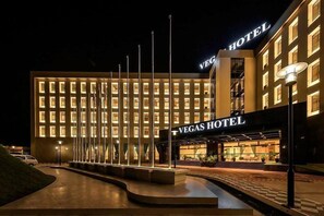The exterior of the Vegas Hotel with a well-lit facade, a prominent entrance, and a series of flagpoles.