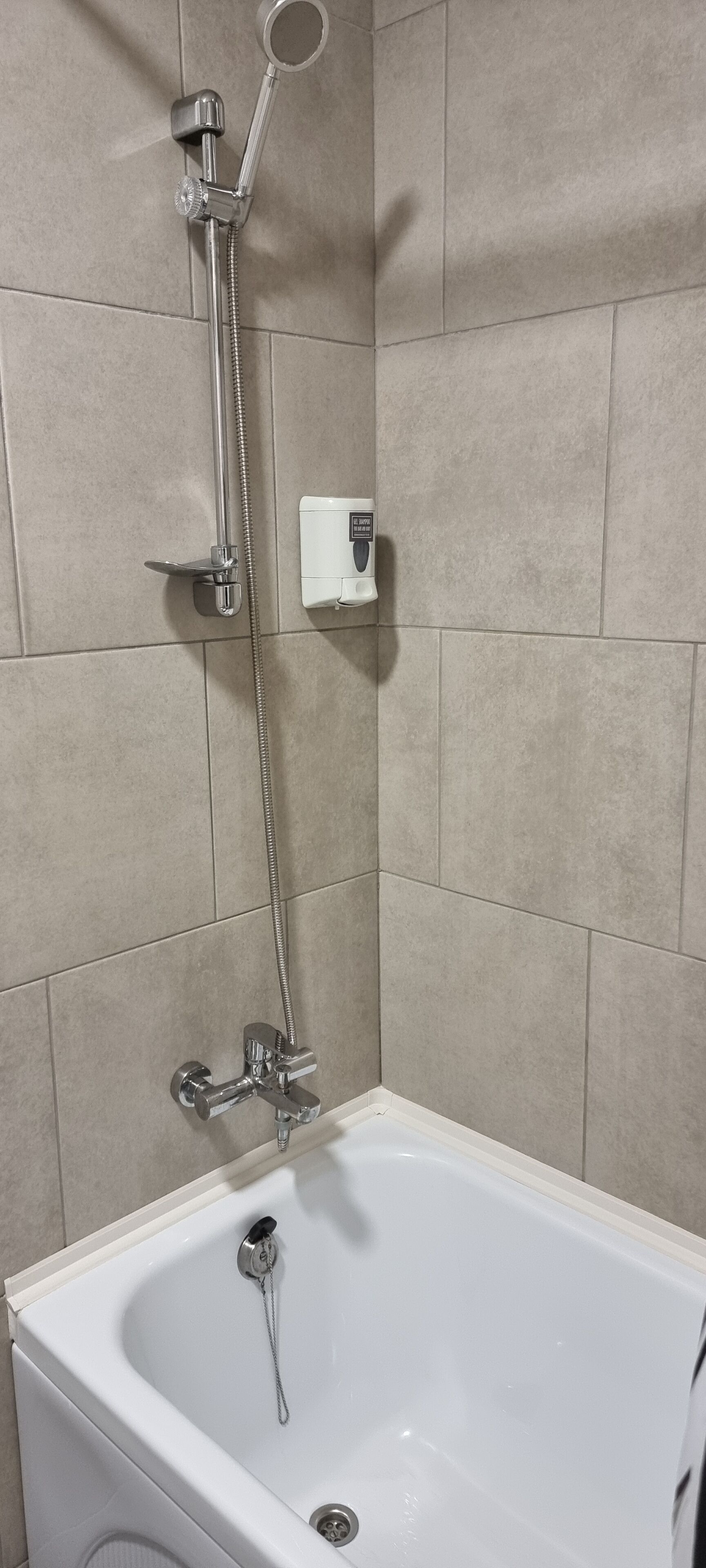 Een badkamer met een bad, een handdouche en een bedieningspaneel aan de muur.