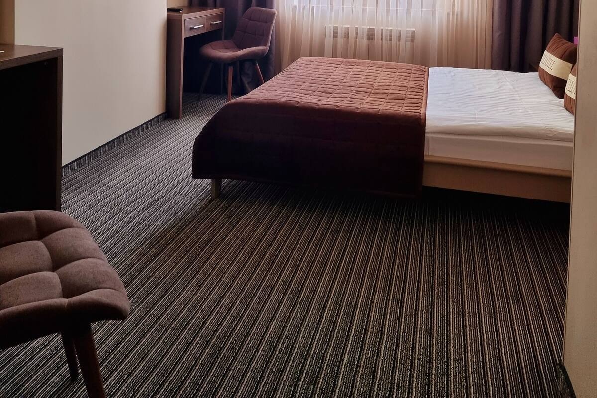 Ein Hotelzimmer mit einem Bett, einem Schreibtisch, einem Sessel, einem Fernseher und einem fensterbepflanzten Fenster.