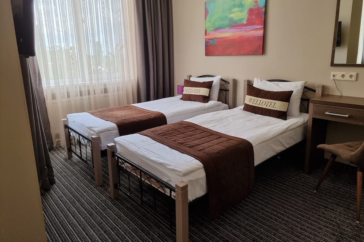 Ein Hotelzimmer mit zwei Betten, einem Schreibtisch, einem Stuhl, einem Fernseher und einem Bild an der Wand.
