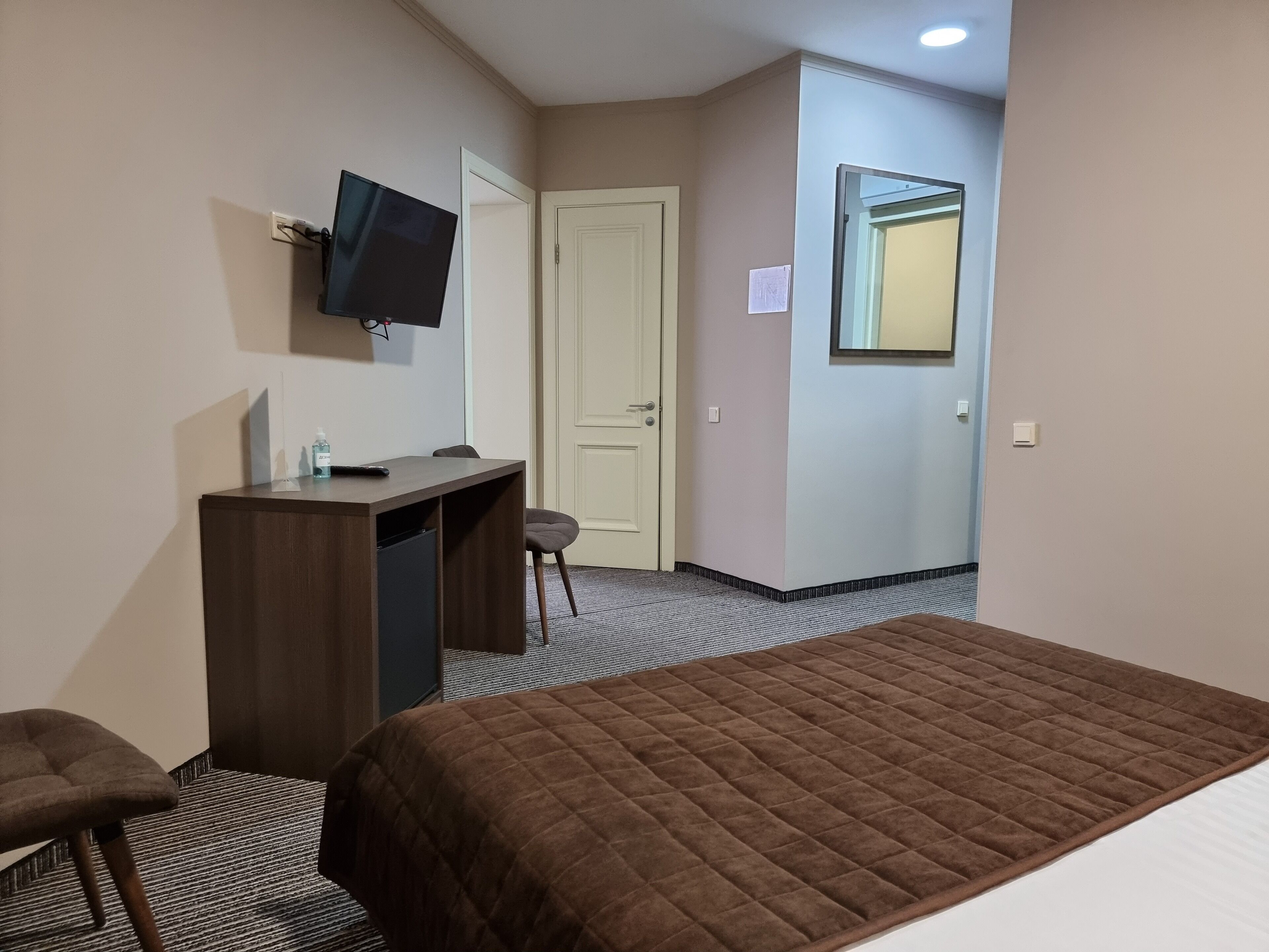 Ett hotellrum med en säng, ett skrivbord, en stol, en tv och en dörr.