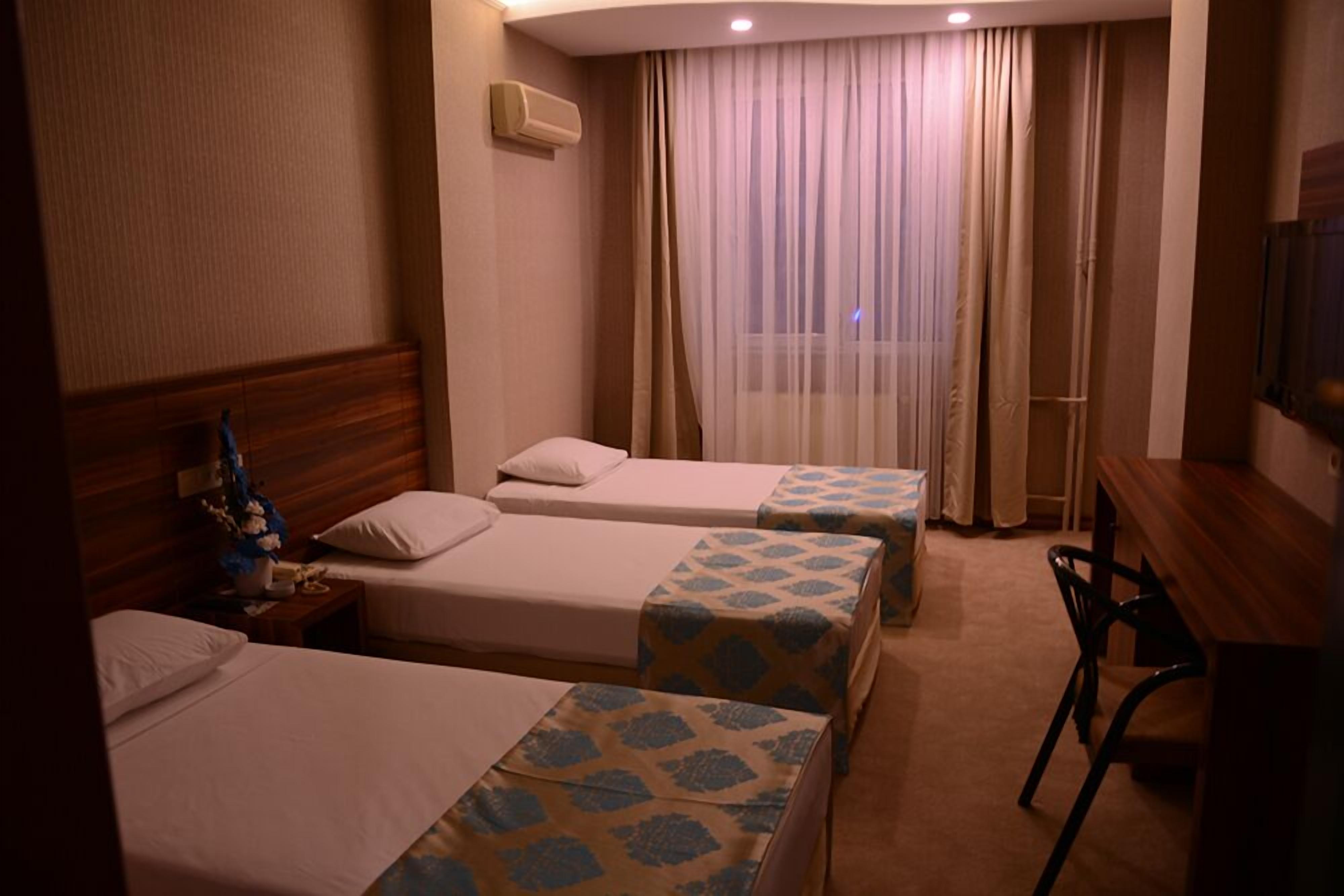A hotel room with two single beds, a wooden headboard, a desk with a chair, and a large window with curtains.