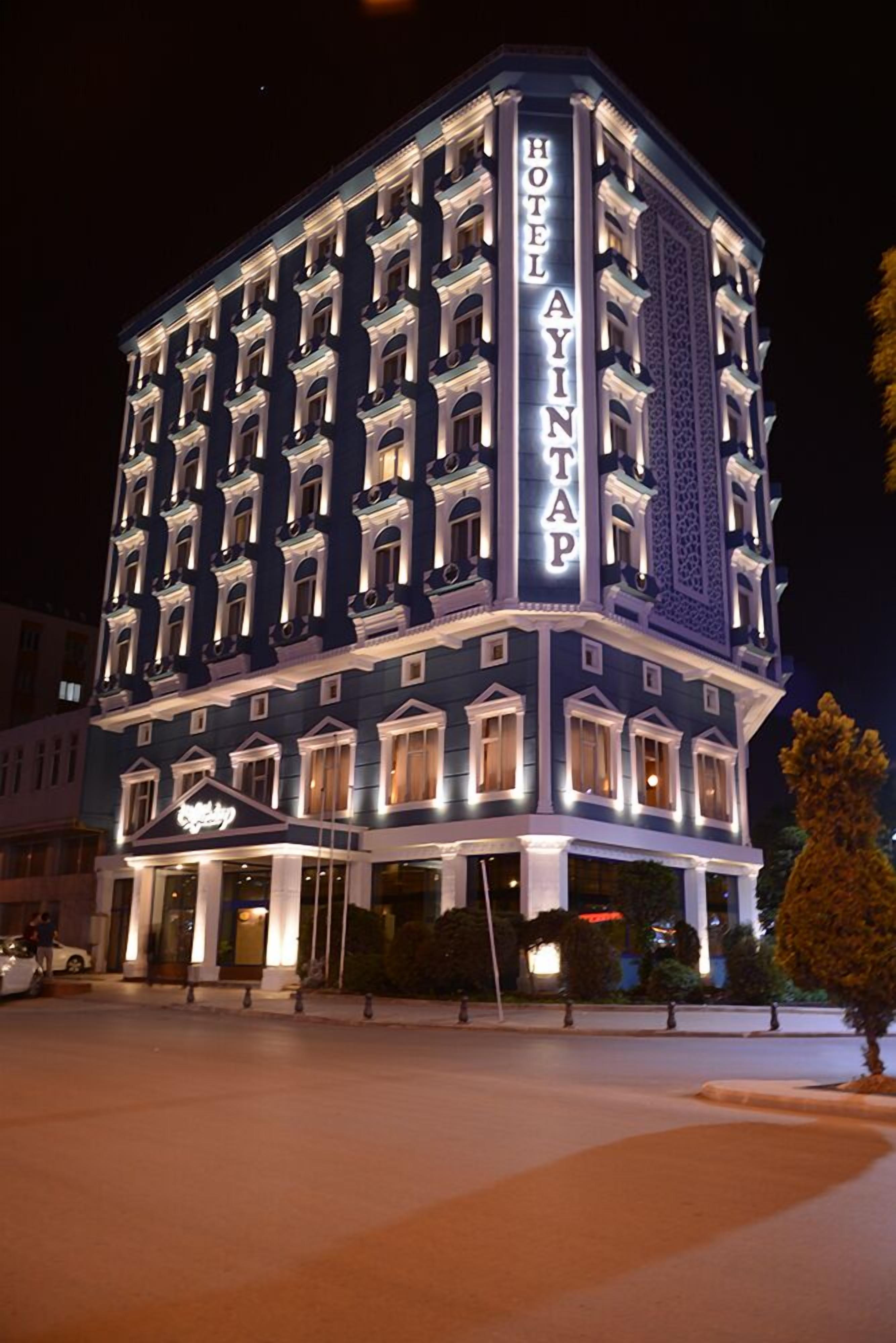 A multi-story hotel with a classic architectural style, featuring a prominent entrance and a sign that reads "HOTEL AYINAP."