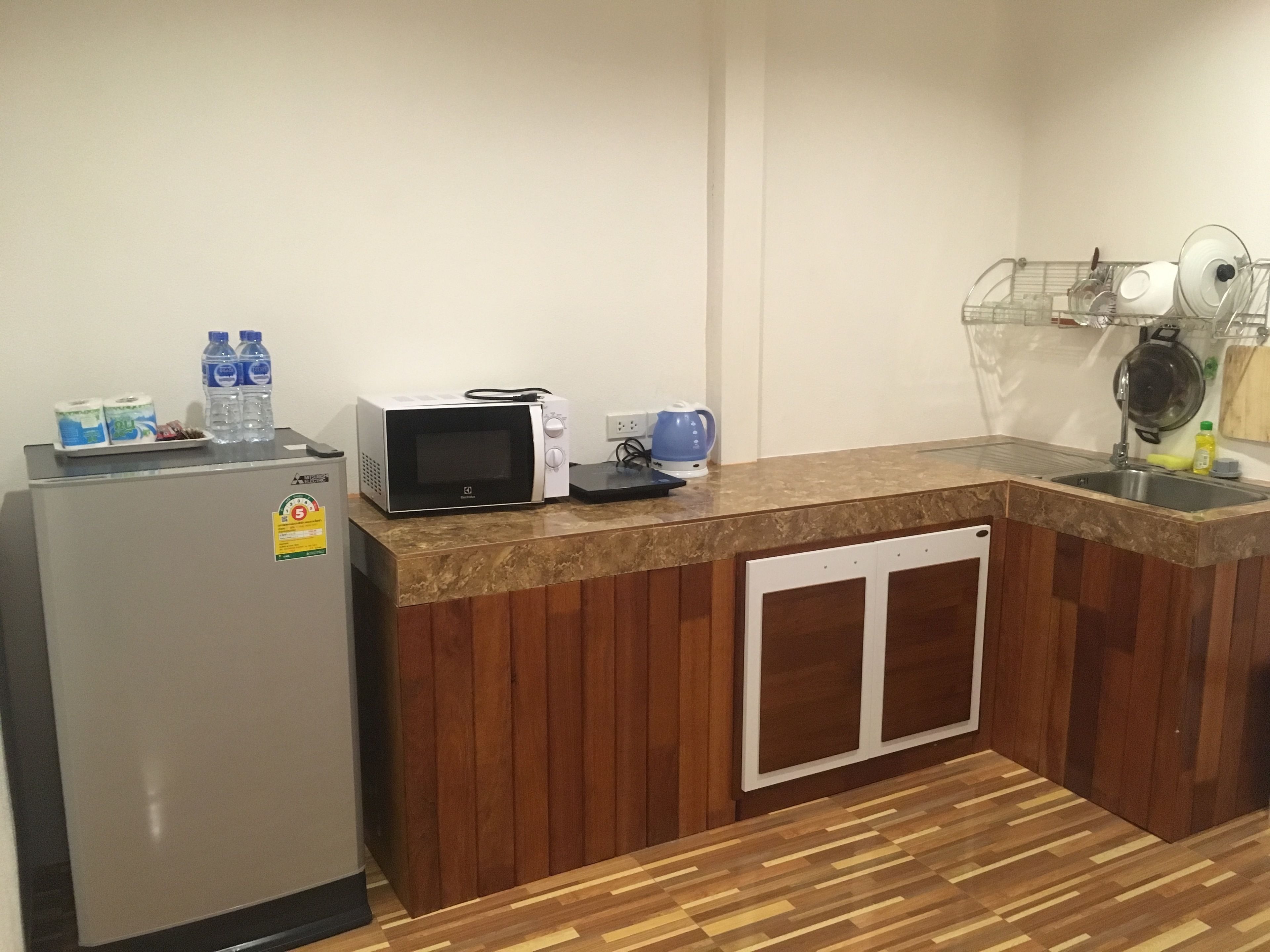 A compact kitchen with a refrigerator, microwave, kettle, and a sink.