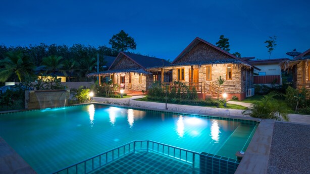 Un resort con piscina, cabañas de techo de paja y exuberante vegetación.
