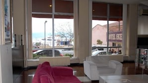 Habitación de hotel con un ventanal grande, un sofá rojo, sillones blancos y un televisor de pantalla plana.