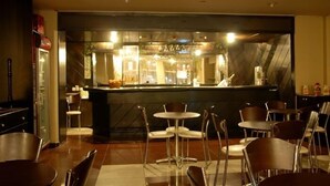 Un restaurante con zona de bar, varias mesas y sillas, y un mostrador con una persona detrás.