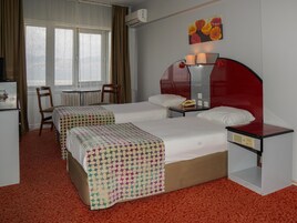 Quarto de hotel com duas camas, uma escrivaninha, uma cadeira, uma mesa e uma janela com cortinas.