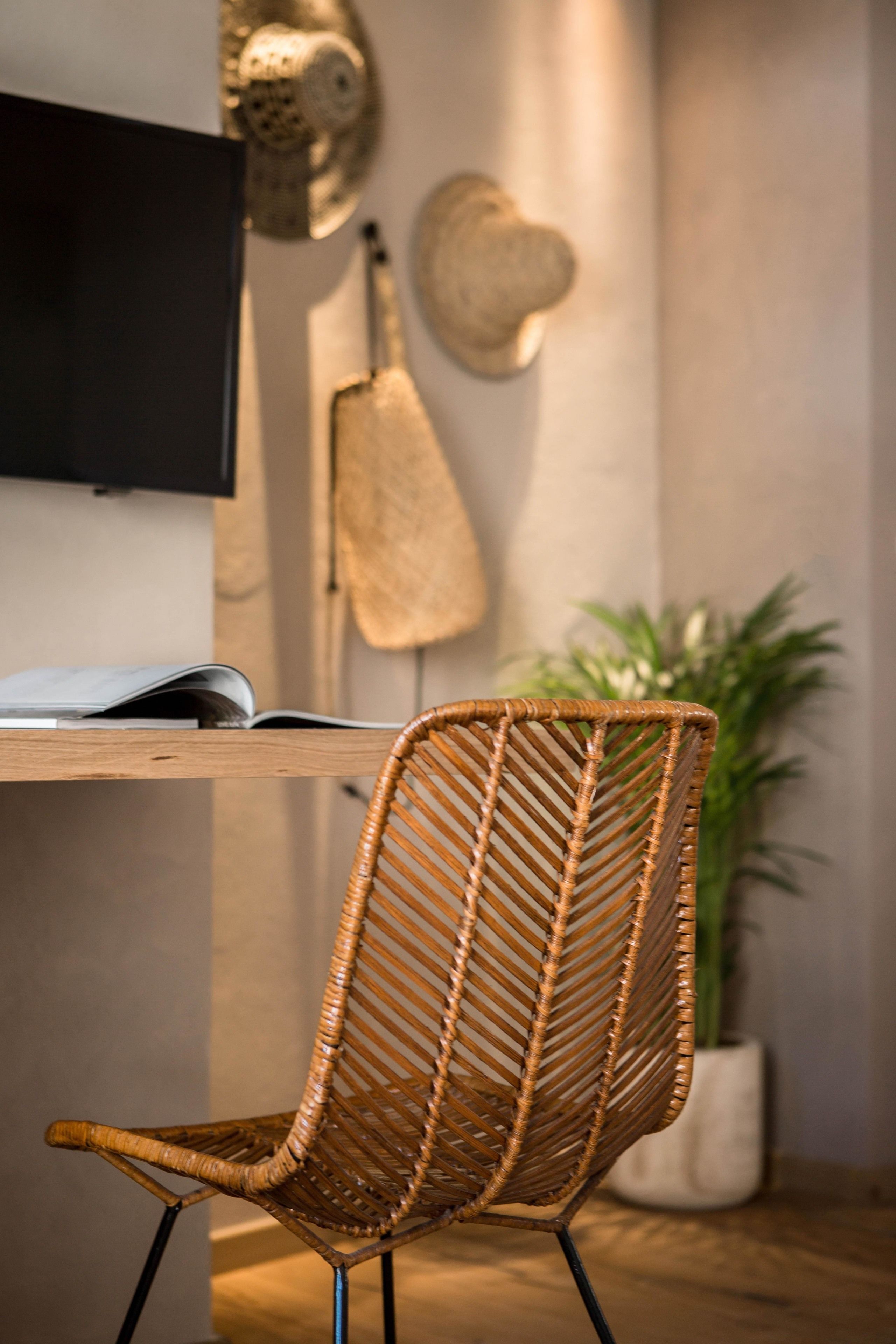 A wicker chair with a unique woven backrest, a flat-screen TV mounted on the wall, and a guitar leaning against the wall.