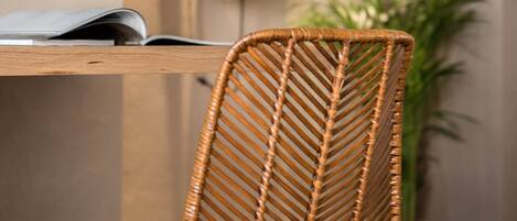 A wicker chair with a unique woven backrest, a flat-screen TV mounted on the wall, and a guitar leaning against the wall.