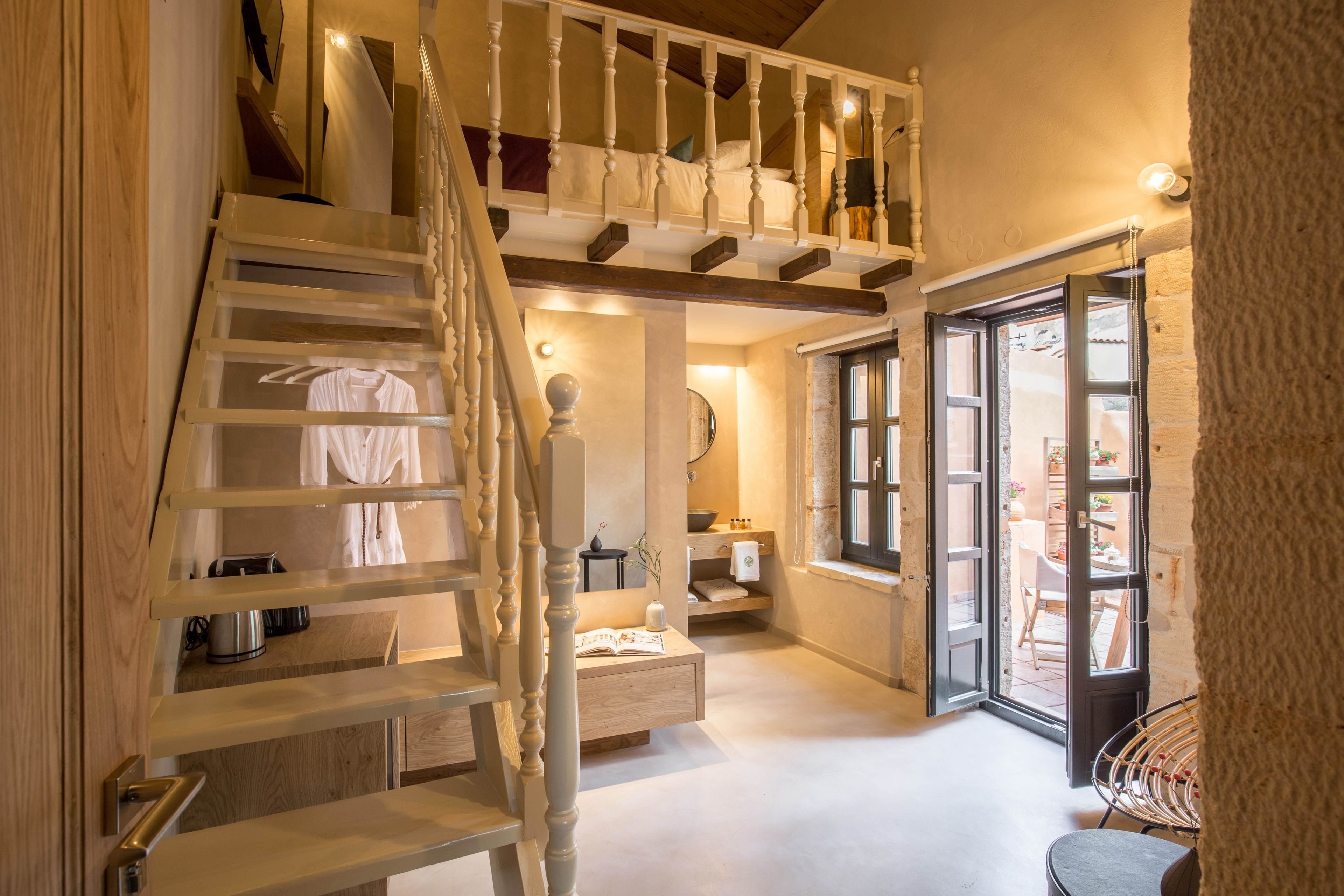 A spacious interior with a wooden staircase, a small sitting area, and a view of the outside.