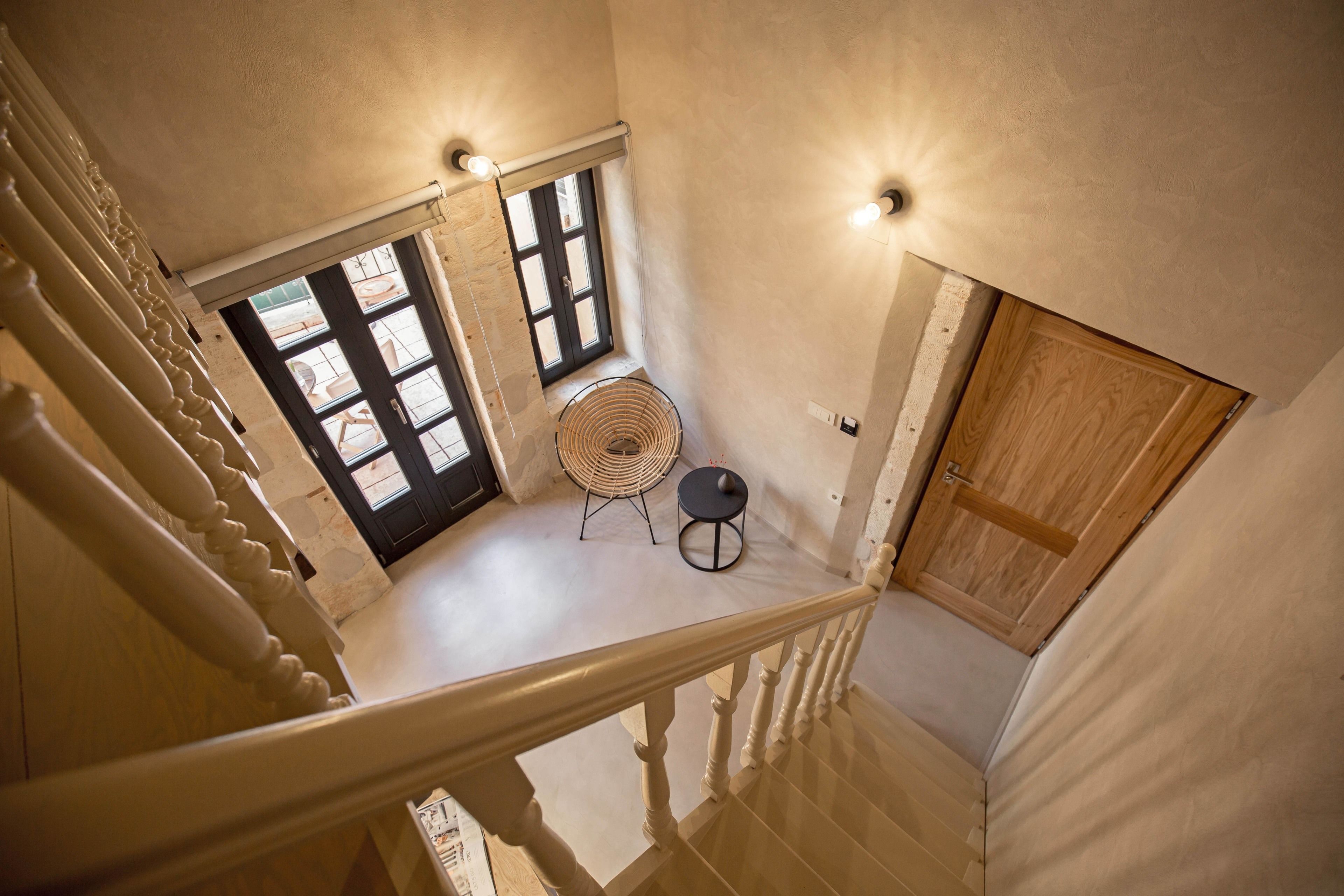 Una escalera con barandilla de madera, una puerta negra y una ventana con persianas.