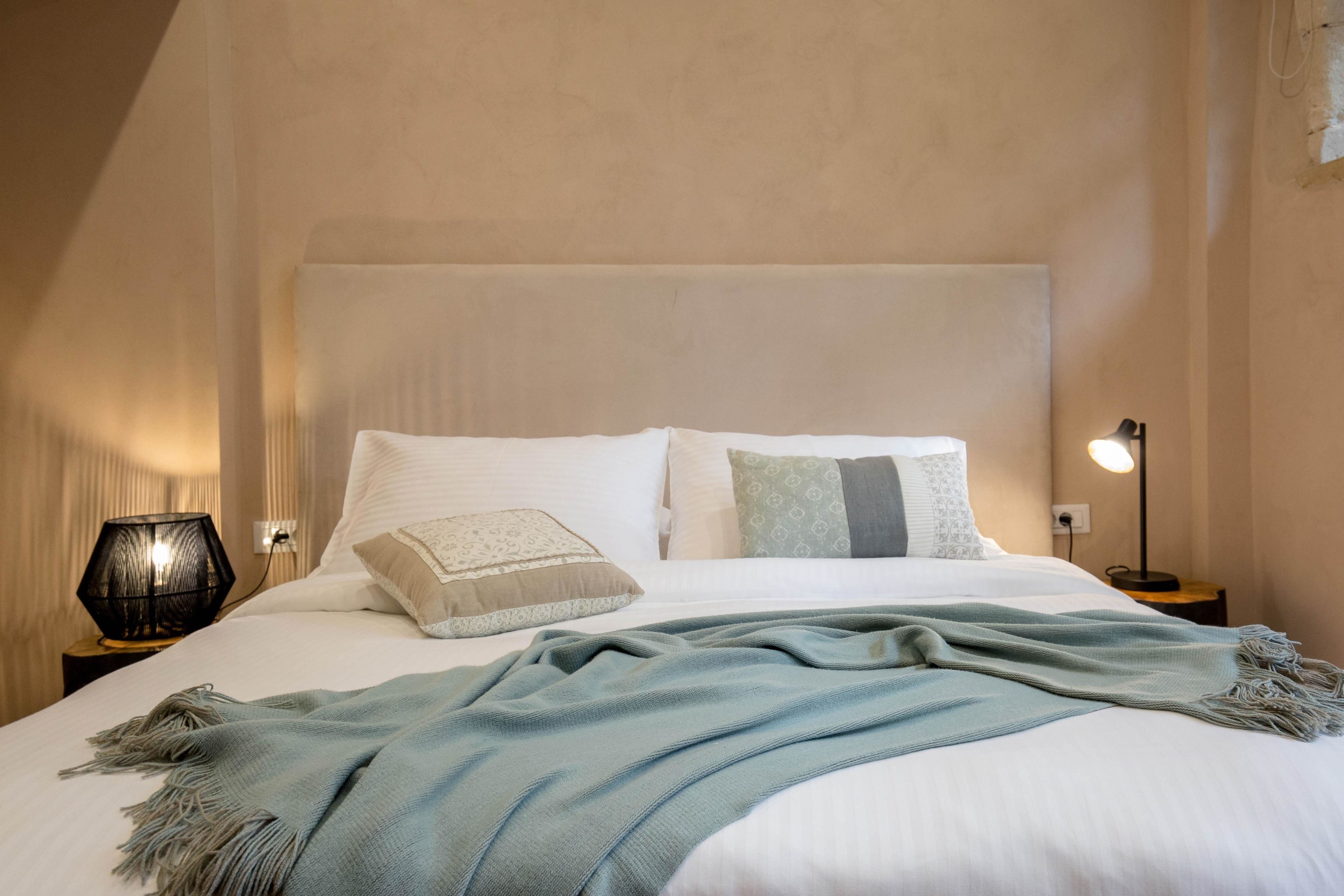 A neatly made bed with a light blue throw blanket, two pillows, and a bedside lamp on a nightstand.