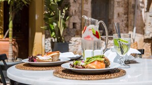 Une table dressée avec des assiettes remplies de nourriture, une carafe de boisson fraîche aux fruits et un verre de boisson fraîche à la menthe.