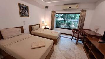 A hotel room with two beds, a desk, a chair, a window with curtains, and an air conditioner.