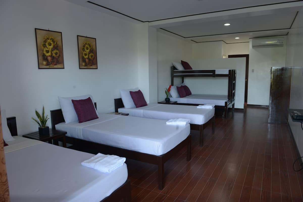 A hotel room with four single beds, a bunk bed, and a small table with a plant.