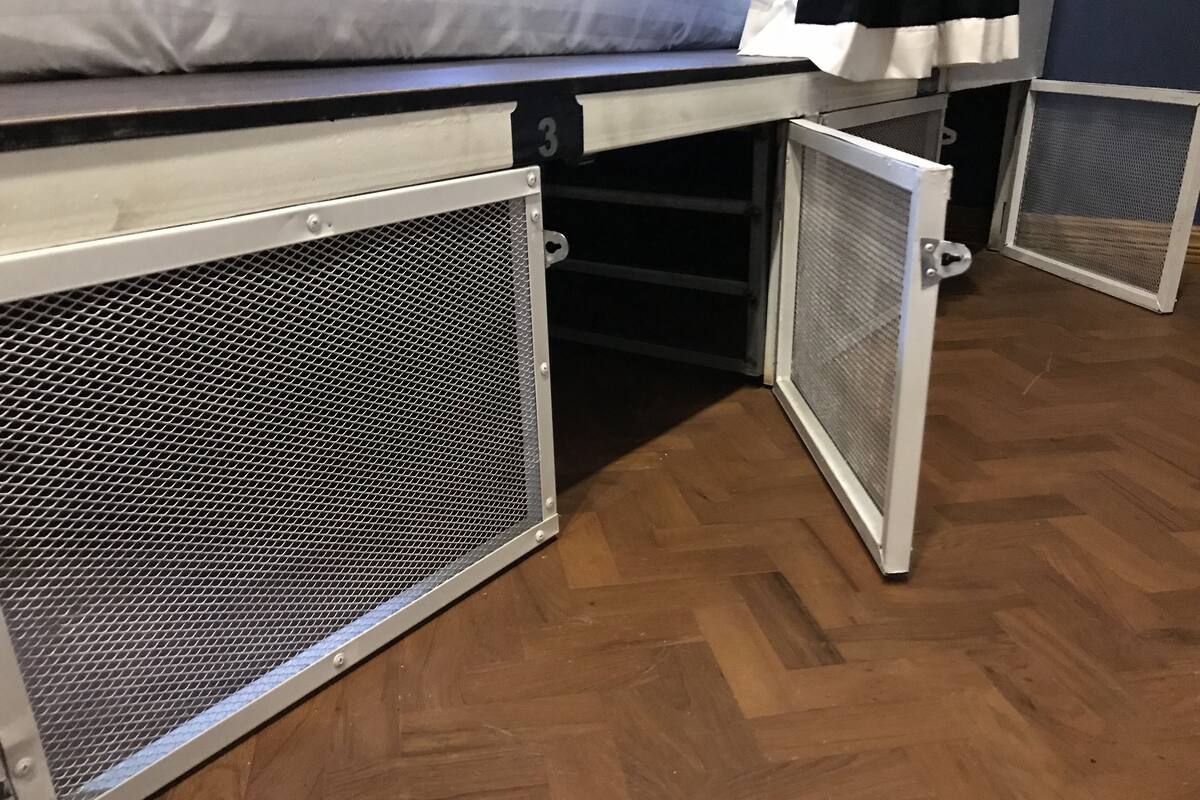 Een kamer met een bed, een klein bureau en een opbergmeubel met een gaasdeur.