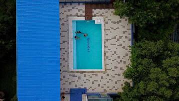 An aerial view of a swimming pool with a tiled deck and a blue roof.