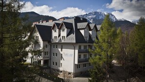 Et hotel i flere etager med klassisk arkitektur, der inkluderer en markant balkon på anden sal og et bjerglandskab i baggrunden.