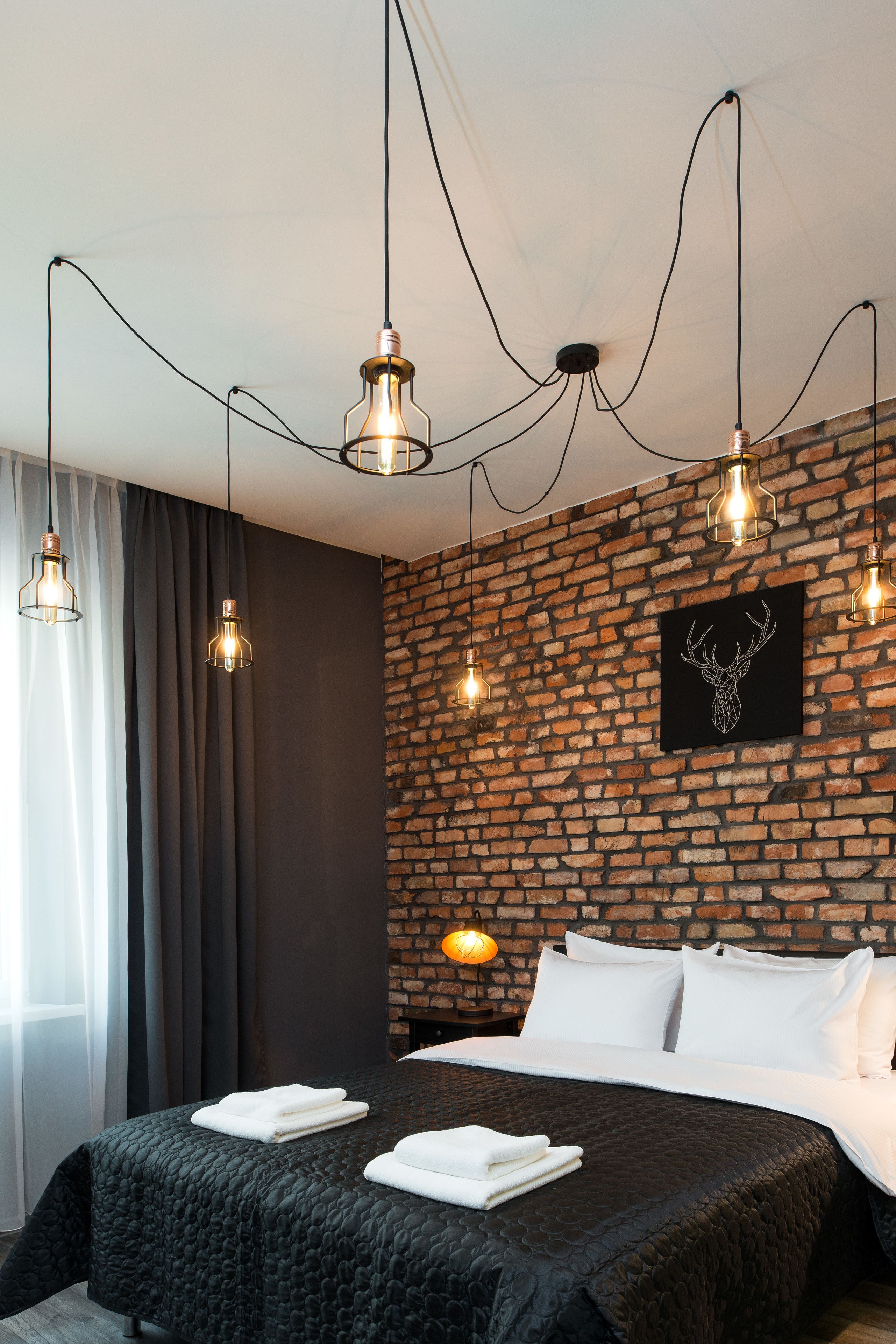 Una camera d'albergo moderna con una parete in mattoni, un letto grande con lenzuola bianche e lampade a sospensione.