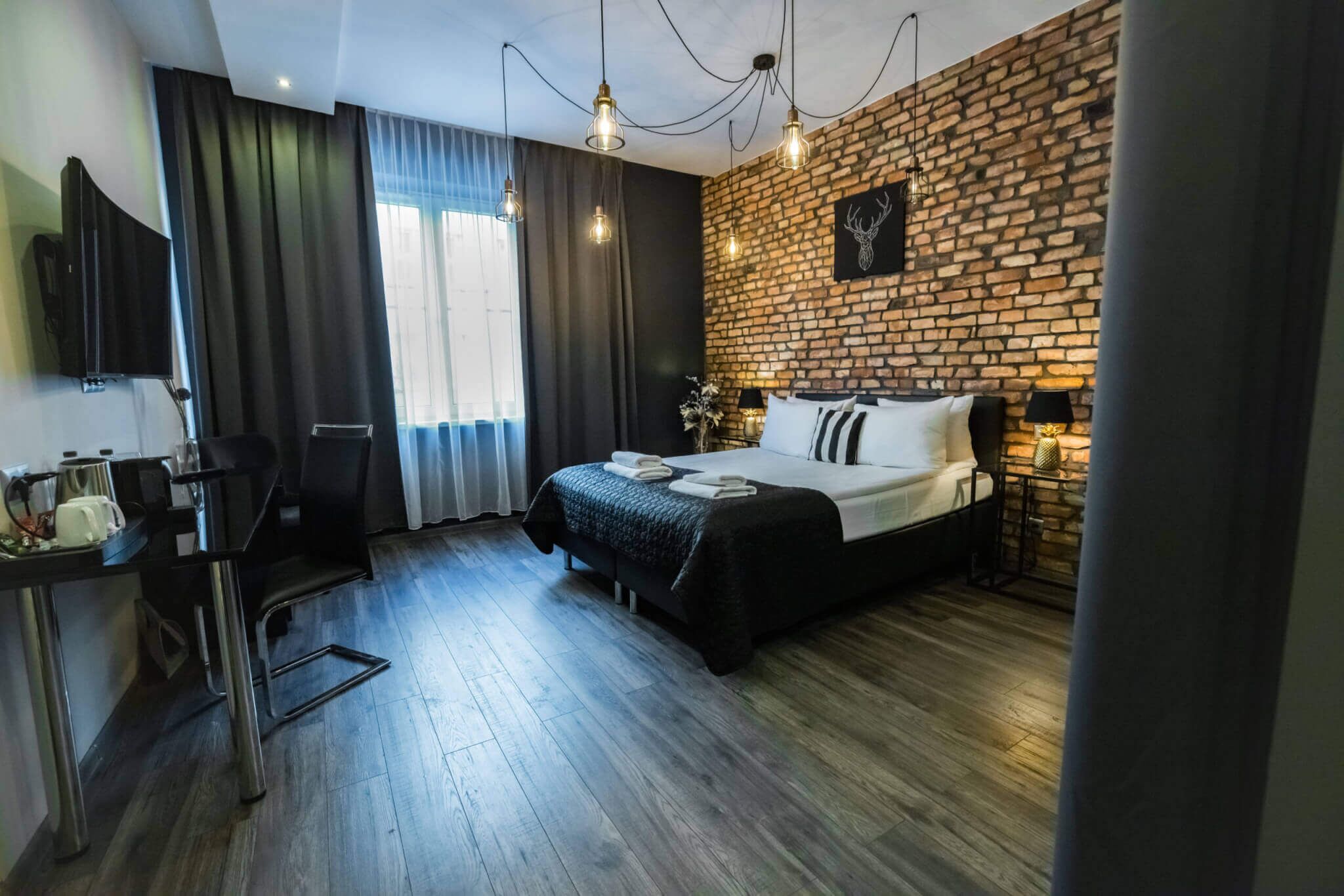 Een moderne hotelkamer met een geaccentueerde bakstenen muur, een groot bed met zwarte beddengoed, een bureau met een stoel en een wandgemonteerde flatscreen-tv.