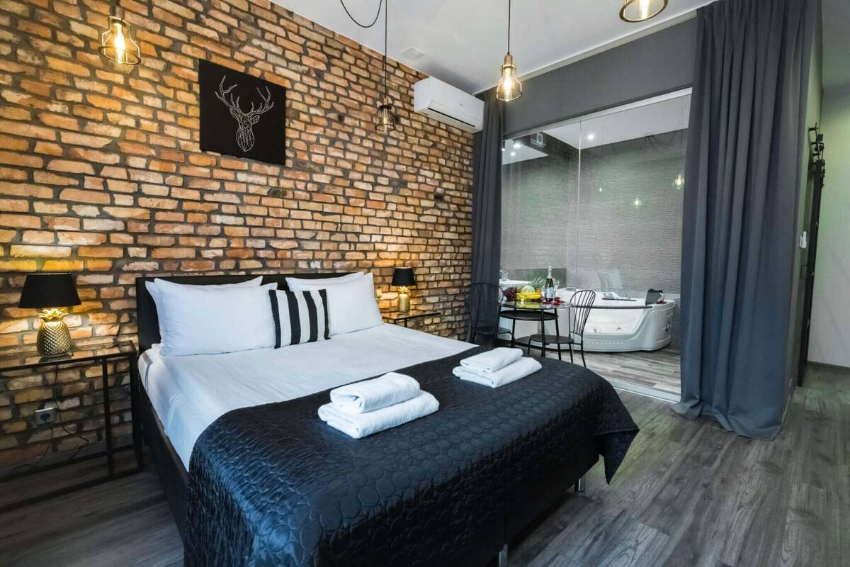 A modern hotel room with a brick wall, a bed with white bedding, two bedside lamps, and a black headboard.