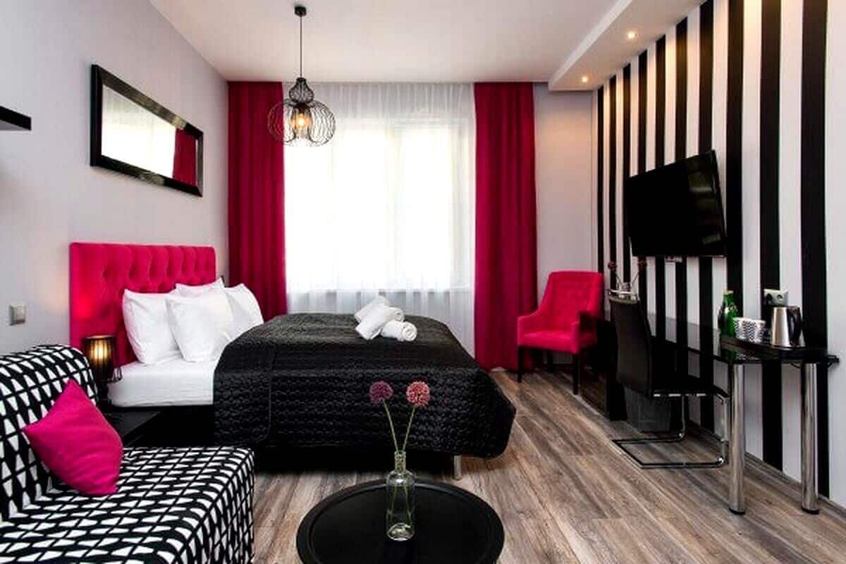A modern hotel room with a bed, a sofa, a TV, and a small table.