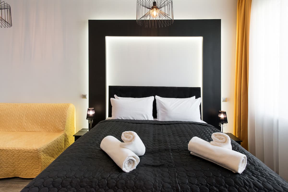 A hotel room with a large bed, two white pillows, a black headboard, and a yellow armchair.