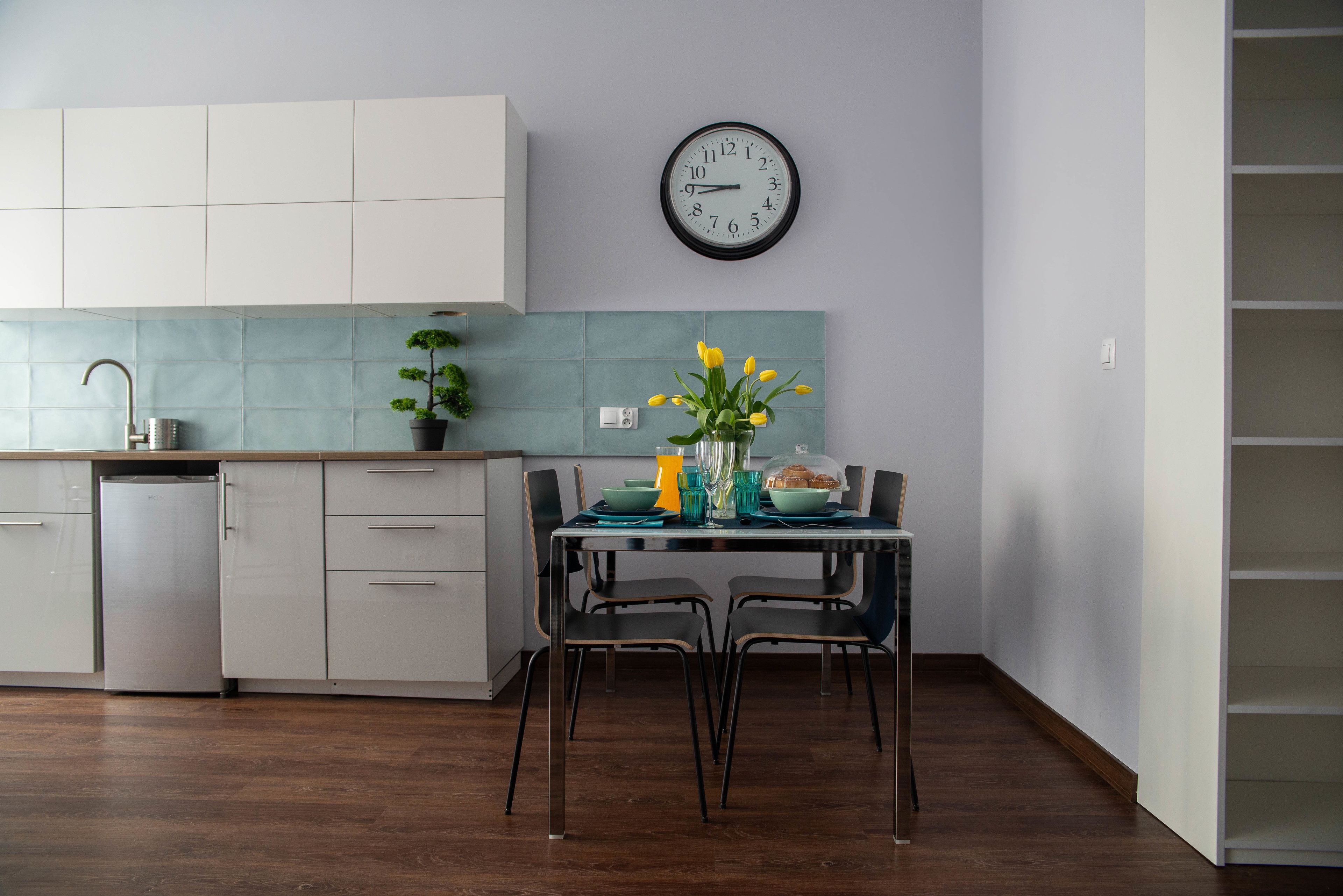A modern kitchen with white cabinets, a sink, and a clock on the wall.