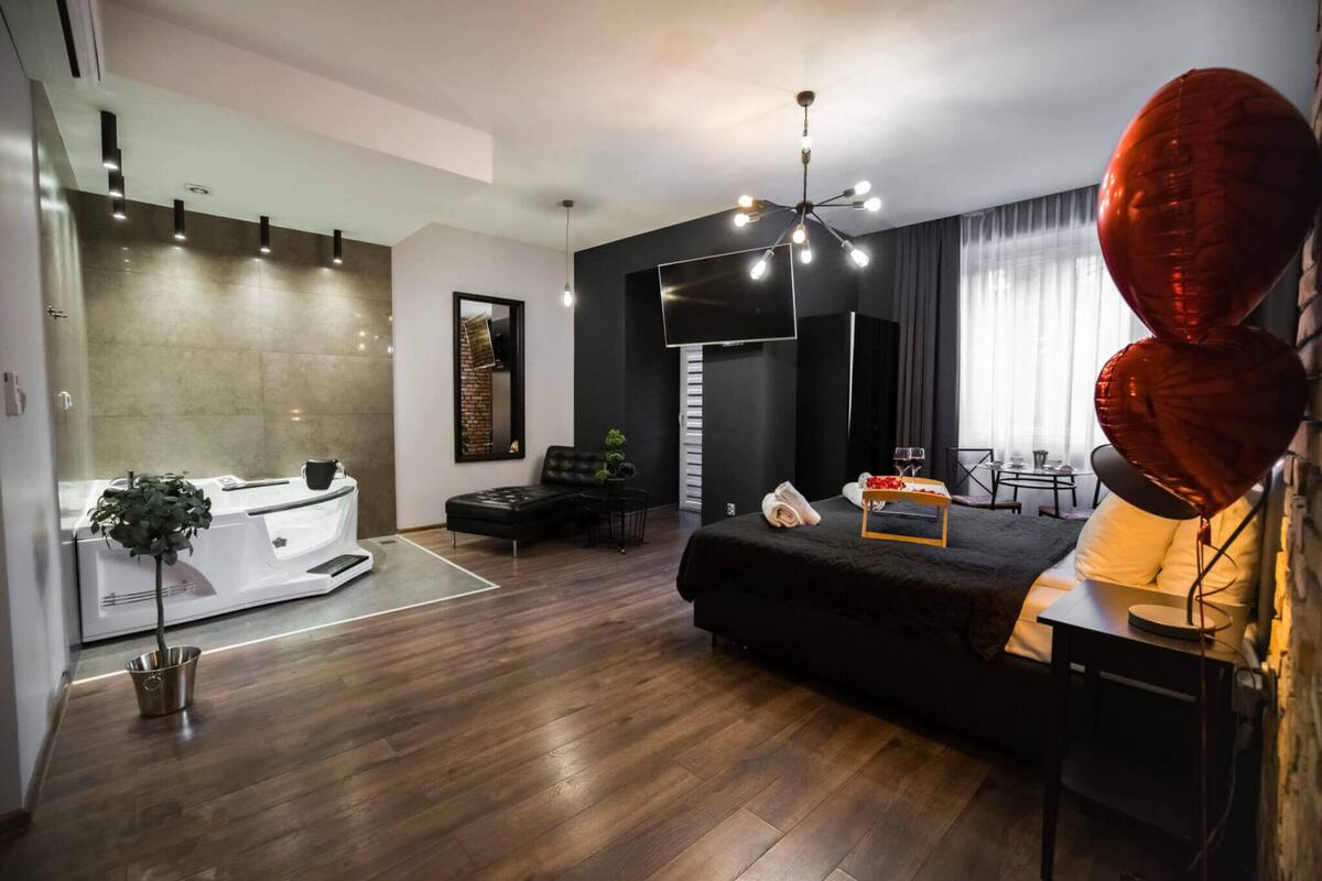 A modern living room with a black sofa, a dining area, and a large TV.