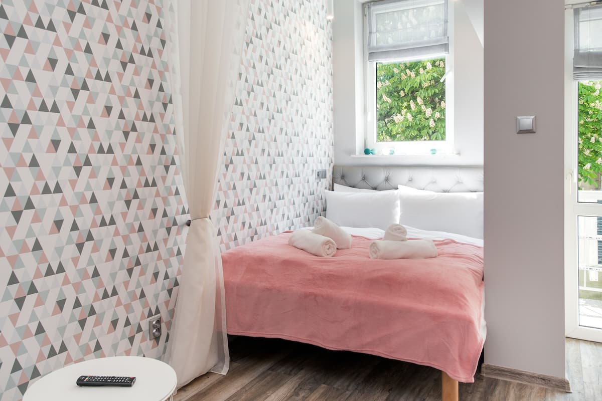 A hotel room with a geometric patterned wall, a pink bedspread, and a window with a view of greenery.