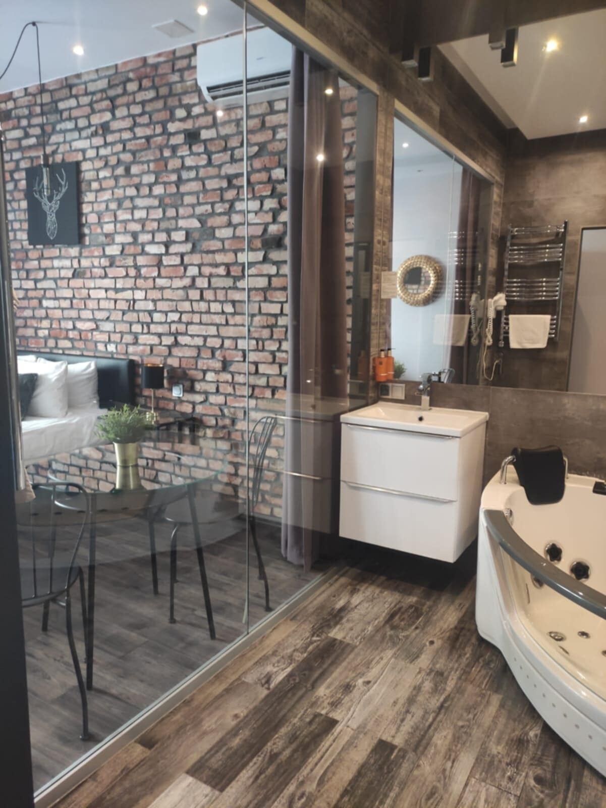 A modern bathroom with a brick wall, a glass partition, a white sink, a bathtub, and a mirror.