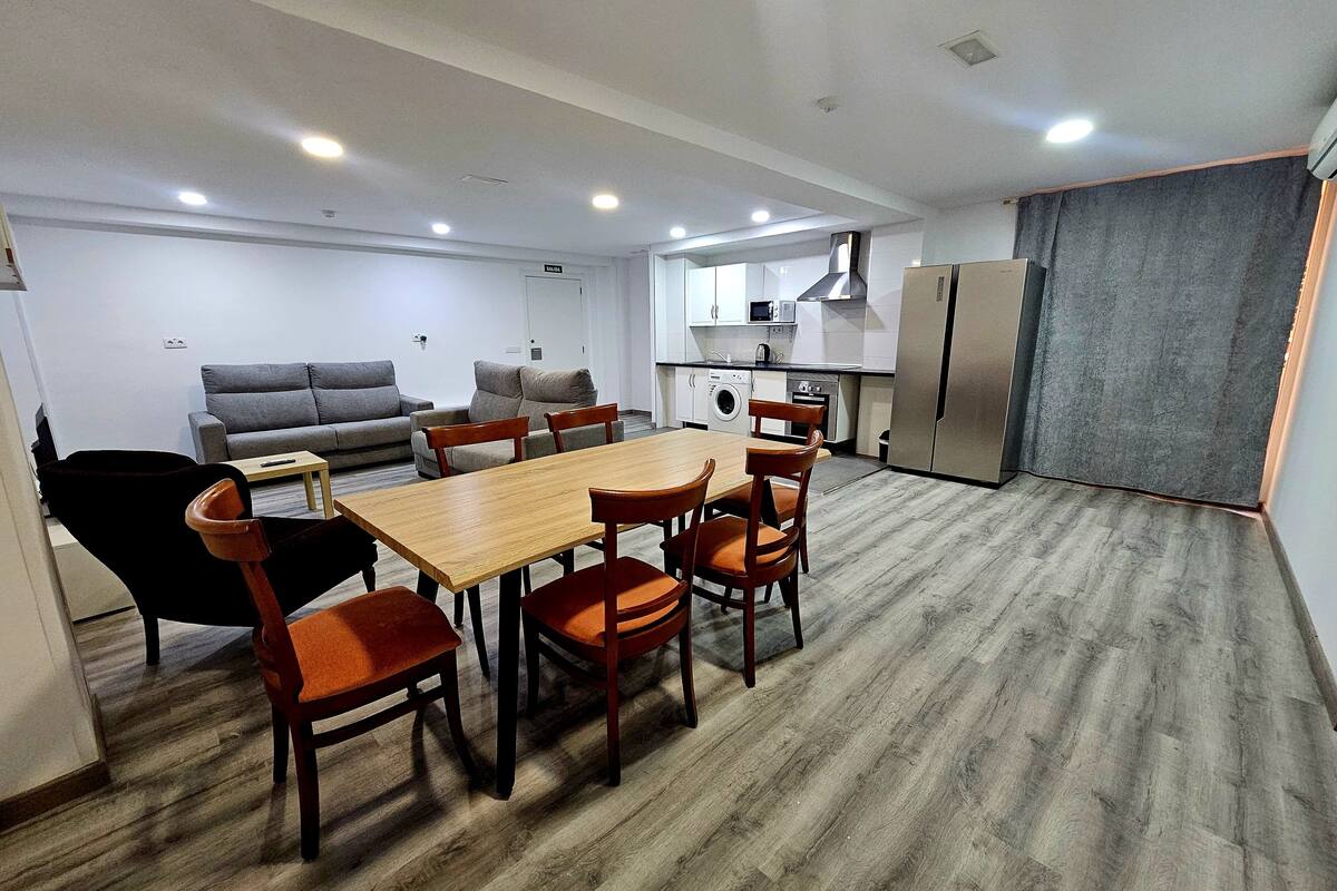 A modern living space with a dining area, sofa, kitchen, and a grey curtain.